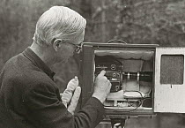 Film-maker Eric Ashby adjusts camera in special box to reduce noise of whirring film camera, 1958. For filming badgers and foxes