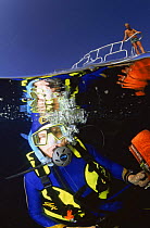 Diver underwater just below surface,  split level  with person standing on boat deck, Egypt