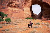 Navajo indian on horseback, in front of eroded hole in red sandstone rock, Monument Valley, Arizona, USA