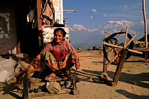 Nepalese woman weaving with Anapurna Mountains behind, near Pokhara, Nepal.