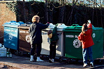 Woman and children putting glass bottles in recycling bins. England, UK