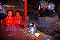 Two girls and elder sitting inside yurt beside kitchen area. Gobi Desert, Mongolia.