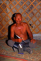 Portrait of man holding pipe inside felt-lined yurt (hut). Gobi Desert, Mongolia.
