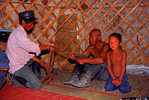 Men and young boy spinning inside yurt (tent), Gobi Desert, Mongolia.