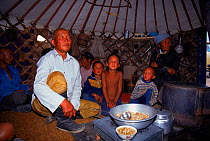 Family sitting in kitchen area inside yurt (tent) about to eat. Gobi Desert, Mongolia.
