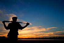 Wildlife ranger with gun silhouetted against sunset sky, Selous Game Reserve, Tanzania.