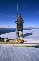 Inuit hunter holding traditional harpoon next to kayak on ice floe, Canadian Arctic
