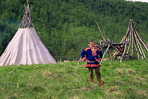 Sami man in traditional clothing, standing in front of lavvu teepee, Lapland, Norway, Europe. 1997.