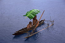 Boys in dugout canoe in rain with palm leaf used as umbrella, Papua New Guinea
