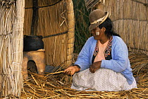 Woman lighting traditional stove on Uros floating reed island, Lake Titicaca, Peru, South America