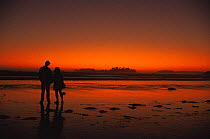 Man and woman against red sky after sunset on sandy beach, British Columbia, Canada