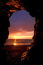 Looking through rock arch to sunset over sea, Church Cove, the Lizard, Cornwall, UK