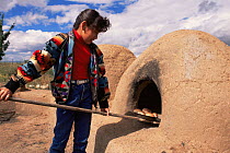 Native American girl taking out bread from traditional oven Taos Pueblo, New Mexico, USA 1990