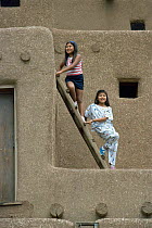 Native American girls on ladder beside traditional home, Taos Pueblo, New Mexico, USA 1990
