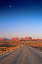 Moon high above disappearing road into Monument Valley Tribal Reserve, Utah, USA
