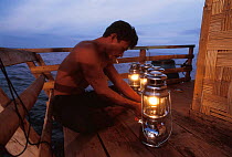 Rakit custodian at Funae fishery raft lights lanterns to attract fish to surface at night for fishermen to catch at dawn. Boats pay to fish in a Rakit area. Custodian spends years living at sea. 2000