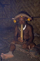 Huli wigman smoking pipe inside hut, in traditional clothing, Papua New Guinea 1991