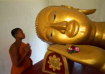 Reclining Buddha and Novice Monk at Wat Pha Baat Tai, Luang Prabang, Laos, South East Asia. Model released.