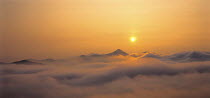Y-9704 Sun setting in evening sky over cloud shrouded mountain peak
