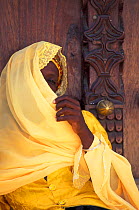 Local muslim woman beside carved studded door. Stone Town, Zanzibar, Tanzania