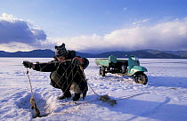 Fisherman fishing through ice on Lake Baikal, Siberia, Russia