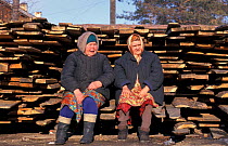 Two women sitting beside pile of timber, Lake Baikal, Siberia, Russia