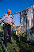Man attending to traditional fishing nets hung out to dry with handmade floats attached, Samiland / Lapland, Finnmark, Northern Norway. 1997.