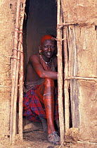 Masai warrior, sitting in hut doorway, Mara, Kenya, decorated with red ochre,