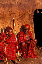 Two Masai elders sit outside hut, during Eunoto ceremony. Mara region, Kenya.