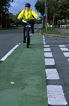Boy cycling home from school in cycle lane on road, UK