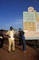 Local giraffe guides waiting for tourists along road by information sign. Sahel, Niger.