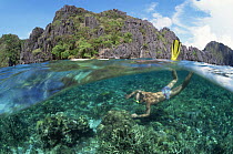 Split level of snorkler diving over coral reef near island, Palawan, Phillippines