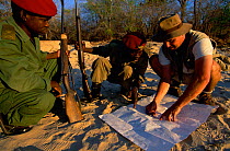 Game warden examines map with armed rangers, Selous GR, Tanzania