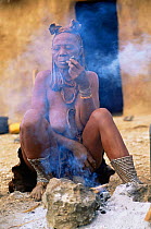 Married Himba woman smoking pipe with Erembe headdress, Kaokoland, Namibia 1999.