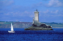 Yacht sails past Vieille lighthouse at entrance to Raz de Seine, Brittany, France
