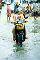 Woman + baby riding scooter in flooded street, HoiAn, Central Vietnam
