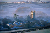 Village landscape in morning mist, Cattistock, Dorset, UK. Church spire, houses and surrounding countryside.