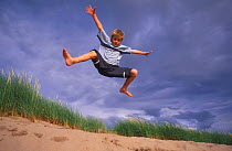 Boy jumping off sand dune, Wester Ross, Scotland, UK.