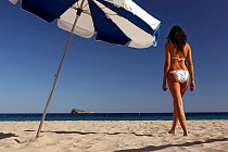 Woman walking along beach with parasol. Playa Poniente, Benidorm, Spain.