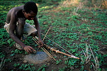 Hadzabe bushman with traditional bow (string made from giraffe tendons)  sharpening arrow. Lake Eyasi, Tanzania.