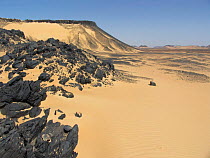 Shiny black volcanic rock strewn over sand in the Black Desert, Western-Egypt.
