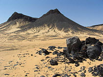 Shiny black volcanic rock strewn over sand in the Black Desert, Western-Egypt.