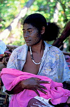 Young Papuan woman with face tattoo breast feeding her baby, Tufi, Oro Province, Papua New Guinea