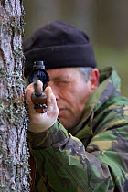 Deer stalker takes aim in pine forest, Highlands, Scotland, UK. Model released.