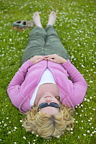 Woman lying in field of daisies enjoying nature on a summer day, Cairngorms National Park, Scotland, Europe Model released.