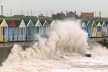 Waves crashing against sea wall near beach huts, Southwold, Suffolk, UK.