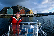 Martin Dahle at  wheel of his boat with decorative wooden houses behind, Trondelag, Norway