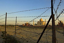 The Taj Mahal viewed through barbed wire fence, from the opposite bank of the Yamuna River. Agra, India.