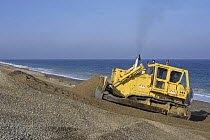 Digger repairing coastal shingle bank, Cley, Norfolk, UK