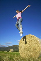 Girl jumping off round hay bale, Scotland, UK Model released.
